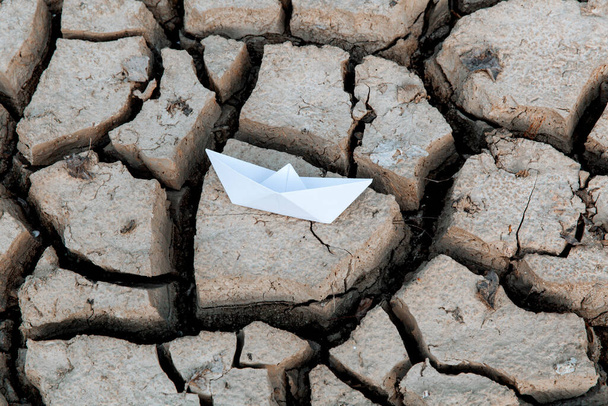 乾燥した乾燥した乾燥した土の上の白い紙のボート。地球温暖化の概念 - 写真・画像