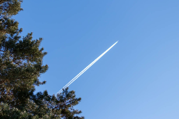 Avión volador en un viaje a través del cielo azul con una pluma de humo blanco largo y chorro de lavado muestra el transporte internacional y la globalización vacaciones transatlánticas con pilotos - Foto, imagen