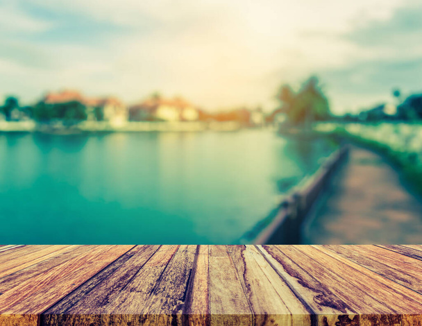 Wood pier or an old wooden table with vintage tone blur image of lake and sunset sky in background - Photo, Image