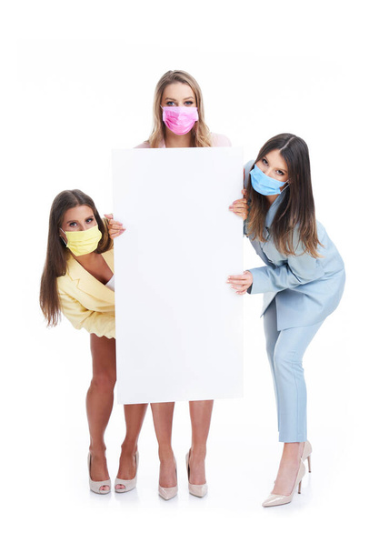 Three women in pastel suits holding billboard posing over white background - Zdjęcie, obraz