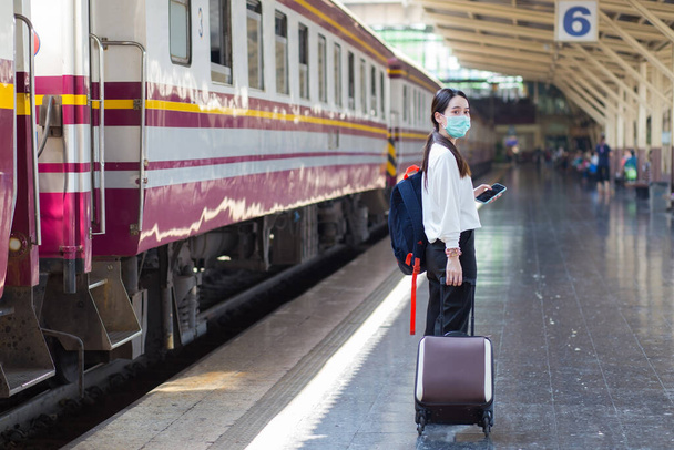 Жінка з Азії тягне свою сумку, щоб подорожувати або повертатися додому поїздом на станції, в той час як вона носить медичну маску як новий нормальний спосіб життя в концепції охорони здоров'я - Фото, зображення