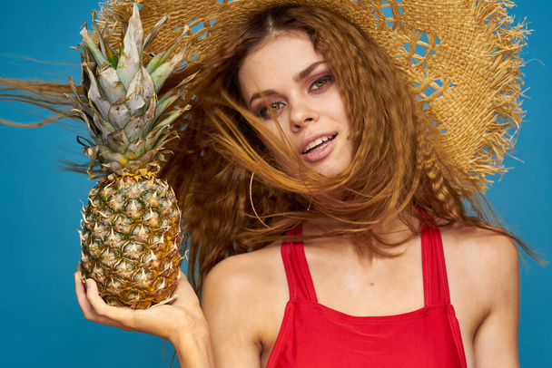Una donna con un cappello di paglia con un ananas tra le mani o è un divertente sfondo di frutta esotica blu - Foto, immagini