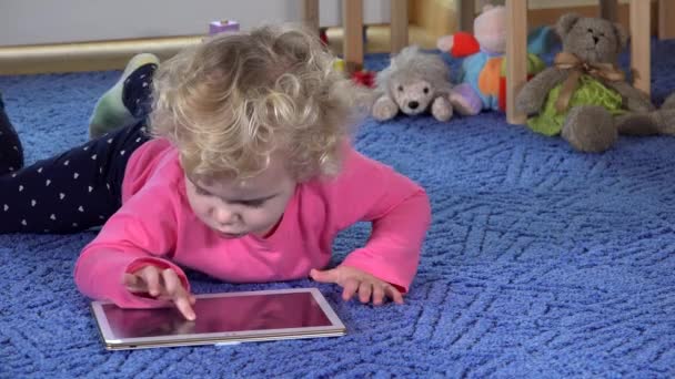 Девушка играет в планшет лежа на голубом ковре. современные медиа-технологии. 4K - Кадры, видео