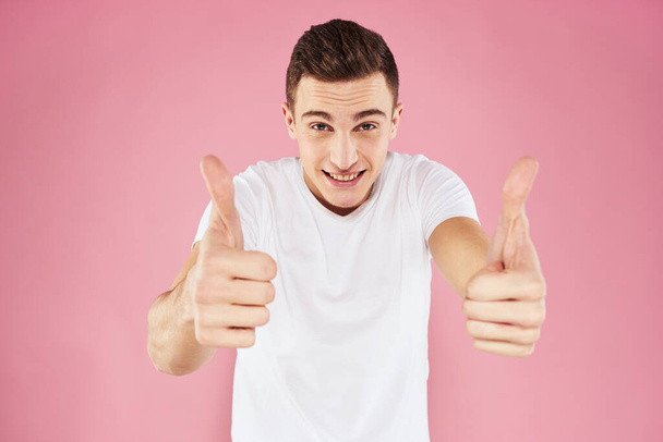 Un hombre con una camiseta blanca gestos con las manos emociones fondo rosa estudio recortado ver - Foto, imagen