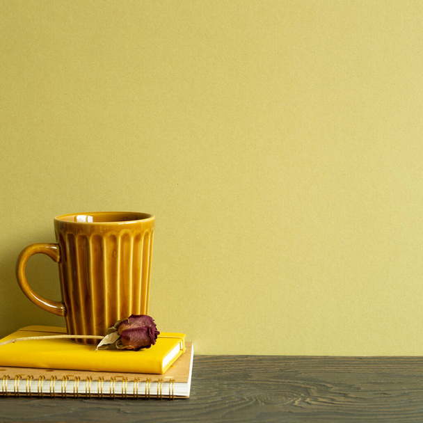 Notebook, mug cup, dry rose on wooden table. khaki background - Photo, Image