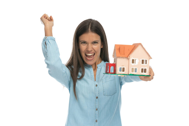 happy casual woman is celebrating succes and holding a house model against white background - Photo, Image