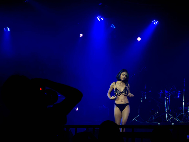 Asiatische sexy Frau in blauem Bikini tanzt Show auf der Bühne auf dunklem Hintergrund mit Bühnenlicht in der Diskothek und Schatten des Fotografen, der Foto im Vordergrund macht, eingerichtete Show. - Foto, Bild