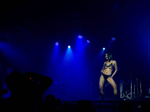 Mujer sexy asiática en bikini azul espectáculo de baile en el escenario sobre fondo oscuro con luz de escenario en la discoteca y sombra de fotógrafo tomando fotos en primer plano, configurar espectáculo. - Foto, Imagen