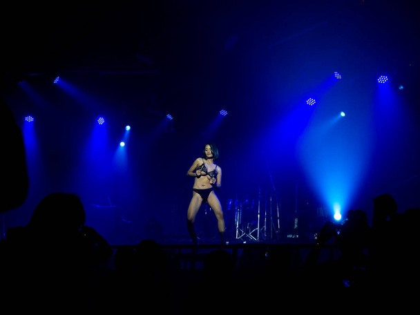 Mujer sexy asiática en bikini azul espectáculo de baile en el escenario sobre fondo oscuro con luz de escenario en la discoteca y sombra de fotógrafo tomando fotos en primer plano, configurar espectáculo. - Foto, imagen