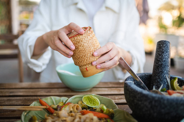 Mulher abrindo recipiente de arroz de bambu pegajoso enquanto tendo uma refeição de três pratos em um restaurante tailandês close-up - Foto, Imagem