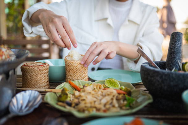 Woman opening sticky rice bamboo container while having a three course meal in a Thai restaurant closeup - Photo, Image