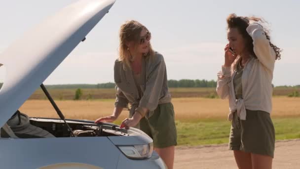 Zwei stylische Freundinnen bei einer Autopanne während der Fahrt an einem sonnigen Tag und rufen nach Pannenhilfe - Filmmaterial, Video