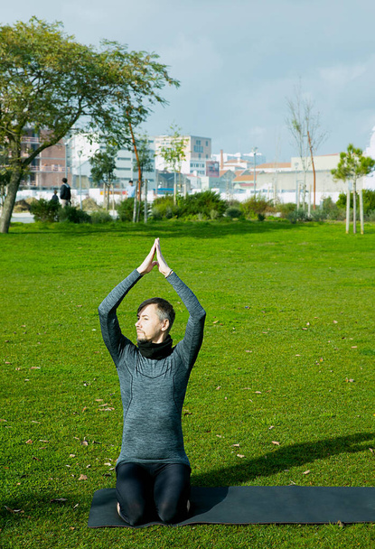 Hombre de mediana edad haciendo respiración, relajación, yoga, estiramiento, exersice, entrenamiento en el parque usando estera de yoga. Posando yoga natural para principiantes. Concepto sanitario. - Foto, Imagen