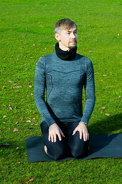 Middle aged man doing breathing, relaxation, yoga, stretching, exersice, workout in the park using yoga mat. Natural beginner yoga posing. Healthcare concept. - Photo, Image