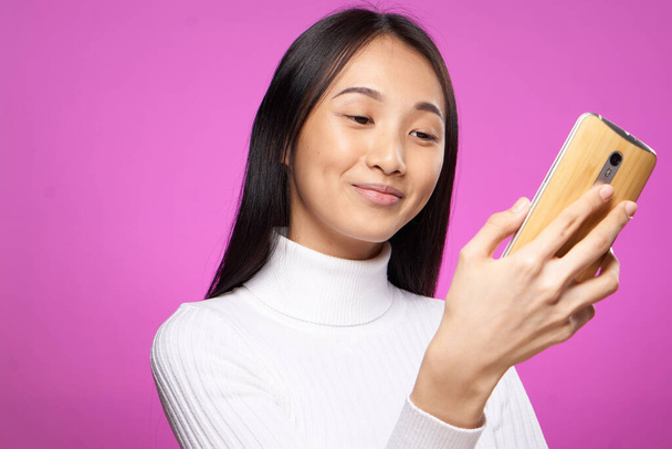 mooie vrouw met telefoon in handen witte trui technologie communicatie roze achtergrond - Foto, afbeelding