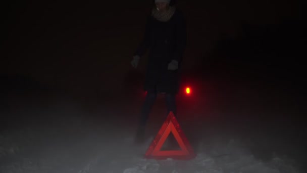 Egy lány felállított egy vészleállító táblát a kocsija mellett egy téli éjszakán.. - Felvétel, videó