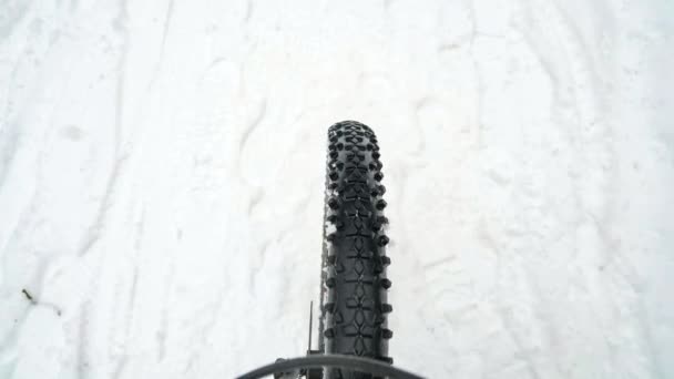La rueda delantera del MTB gira con fuerza y torpemente en nieve pisoteada y congelada. Entrenamiento de invierno en una bicicleta de montaña, bosque pista única. - Imágenes, Vídeo