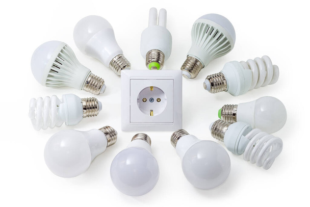 Mehrere Haushalts-Leuchtdiodenlampen und Kompaktleuchtstofflampen unterschiedlicher Bauart rund um die Steckdose auf weißem Hintergrund ausgelegt - Foto, Bild