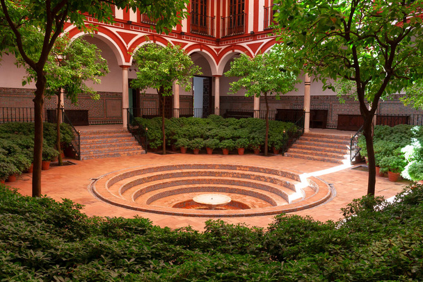 Andaluzyjski dziedziniec otoczony łukami i kolumnami z okrągłą fontanną schodkową w centrum. Sewilla, Andaluzja, Hiszpania. - Zdjęcie, obraz