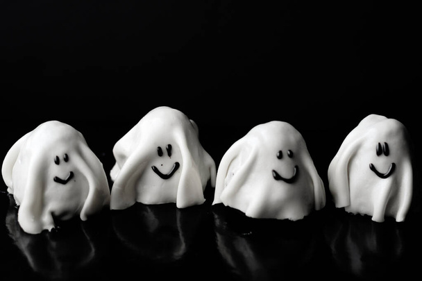 Halloween Concept - neljä pientä valkoista aavetta hymyillen. Herkullisia kakkuja Halloween vastaan musta tausta kopioi tilaa. - Valokuva, kuva