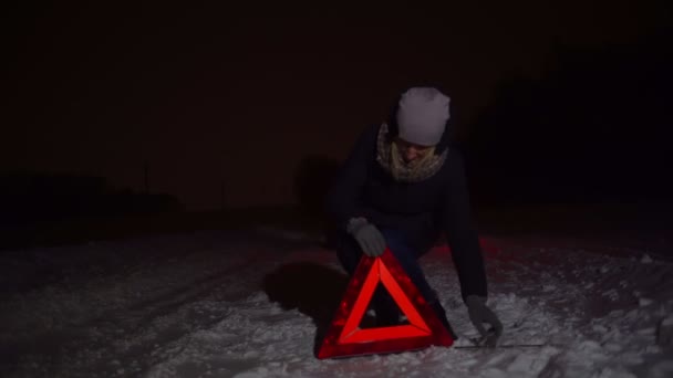 una chica pone una señal de parada de emergencia junto a su coche en una noche de invierno. - Metraje, vídeo