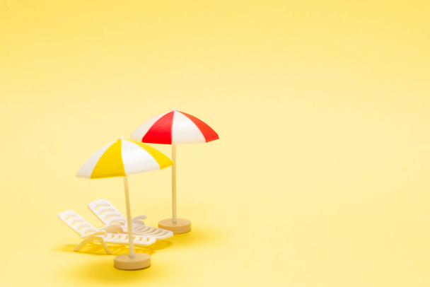 Dos tumbonas y un paraguas rojo sobre fondo amarillo. Copiar espacio. - Foto, imagen