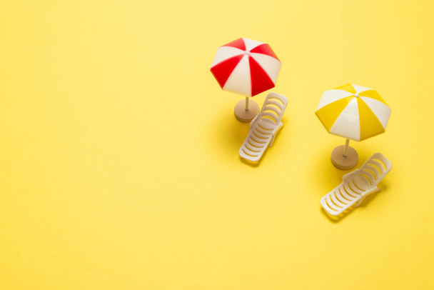 Δύο ξαπλώστρες και μια κόκκινη ομπρέλα σε κίτρινο φόντο. Αντιγραφή χώρου. - Φωτογραφία, εικόνα