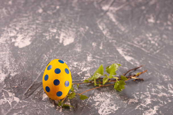 イースター組成-青いエンドウ豆と灰色のテーブルの上に緑の小枝を持つ黄色の卵。テキストのためのスペース、コピースペース - 写真・画像