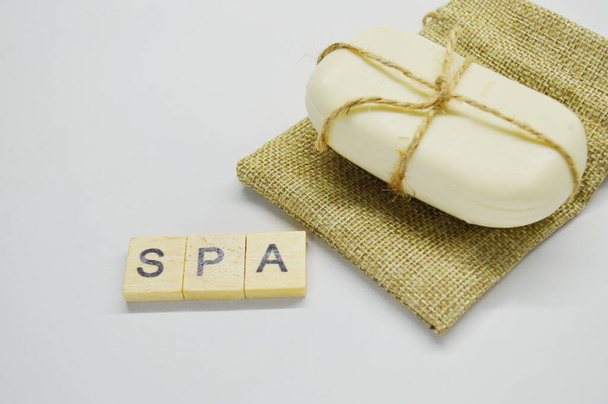 White soap tied with a rope lies on a white background on a jute bag. word Spa made of wooden letters - Photo, Image