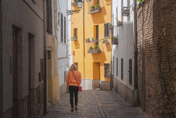 Granada, Endülüs, İspanya 'daki eski kentin dar kaldırım taşlı arka sokaklarını (Albaicin veya Arap Mahallesi) keşfeden sarışın bir bayan turist.. - Fotoğraf, Görsel