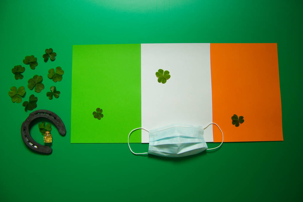 lucky horseshoe with group of three-leaf covers and pot of liquid gold and sanitary mask on green background and flag of ireland - Photo, Image