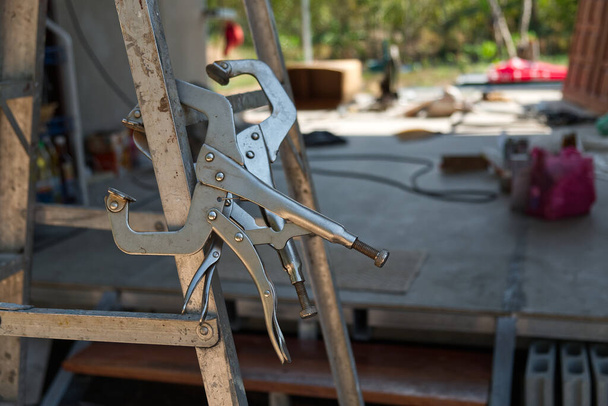 C-Clamp Locking Pliers on the Aluminum Folding Stairs in the Construction Site.  - Photo, Image