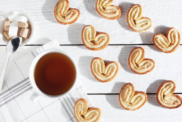 Kalp şeklinde poğaça kurabiyeleri ve beyaz ahşap bir masada bir fincan çay. - Fotoğraf, Görsel