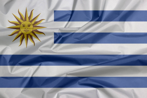 Uruguayská vlajka. Záhyb uruguayské vlajky pozadí, horizontální pruhy bílé střídavě se světle modrou a slunce května. - Fotografie, Obrázek