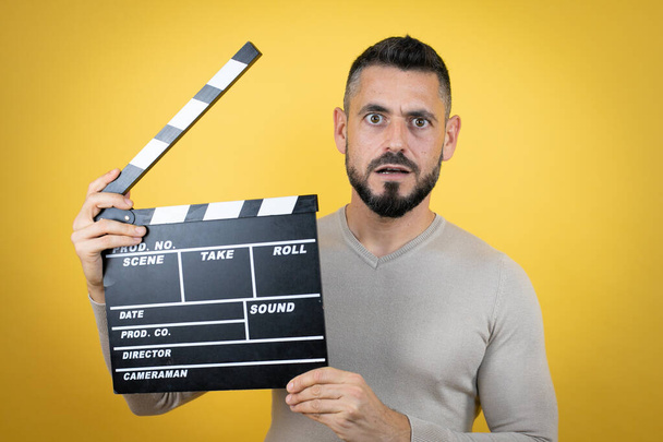 Handsome man with beard wearing sweater over yellow background holding clapperboard very happy having fun - Photo, Image