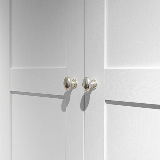 Accesorios para muebles. Puertas metálicas de plata con sombras nítidas en la fachada de madera blanca - Foto, imagen