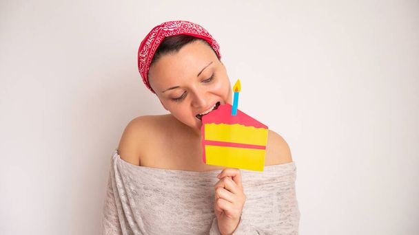 Frau isst falschen Papier-Bastelkuchen auf einem Stock. Porträt einer Frau, die gerne Süßigkeiten isst. Alles Gute zum Geburtstag in Quarantäne. - Foto, Bild