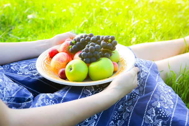 Η γυναίκα κρατάει πιάτο με φρούτα. Κορίτσι στο πράσινο γρασίδι σε μπλε vintage φόρεμα. Ρουστίκ καλοκαιρινό διαμέρισμα θέσει. Υγιεινός χορτοφαγικός οικολογικός τρόπος ζωής. - Φωτογραφία, εικόνα