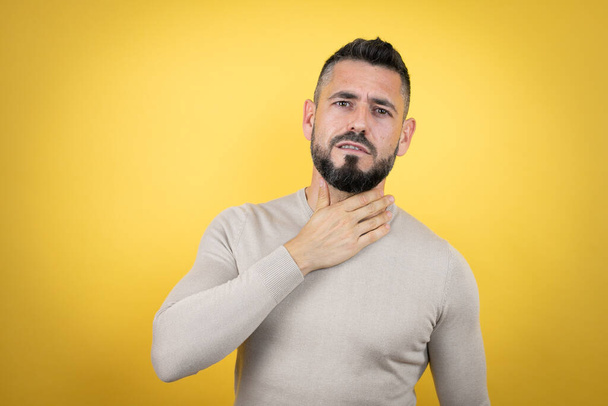 Handsome man with beard wearing sweater over yellow background touching painful neck, sore throat for flu, clod and infection - Photo, Image