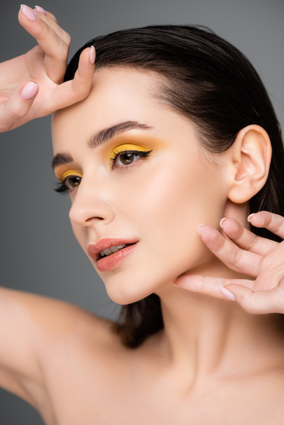 brunette young woman with yellow eyeshadow and lip gloss looking away isolated on grey - Foto, Imagem