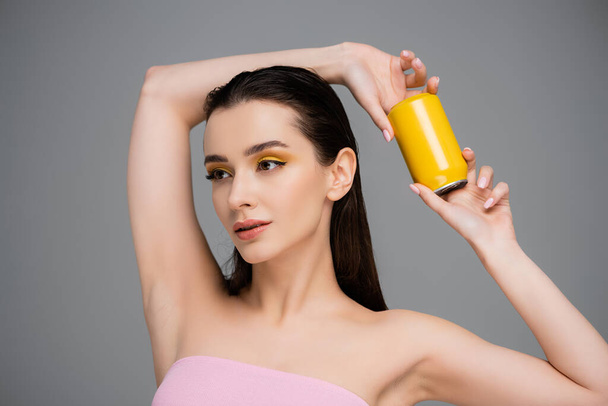 brunetka młoda kobieta z nagie ramiona trzymając żółty puszka z miękki napój odizolowany na szary  - Zdjęcie, obraz