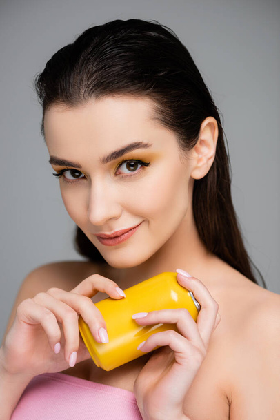 sly young woman holding yellow can with soft drink isolated on grey  - Foto, imagen