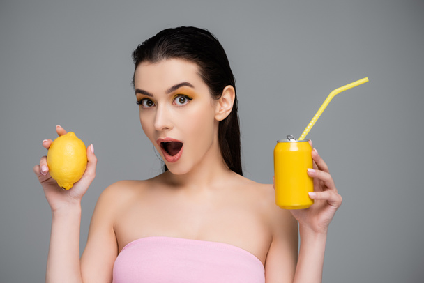 黄色の缶を持っている若い女性を驚かせソフトドリンクとレモンをグレーに隔離し  - 写真・画像