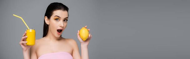amazed young woman holding yellow can with soft drink and lemon isolated on grey, banner  - Photo, Image