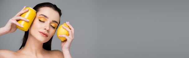 bruna donna con gli occhi chiusi in possesso di lattina gialla con bibita e limone maturo isolato su grigio, banner - Foto, immagini