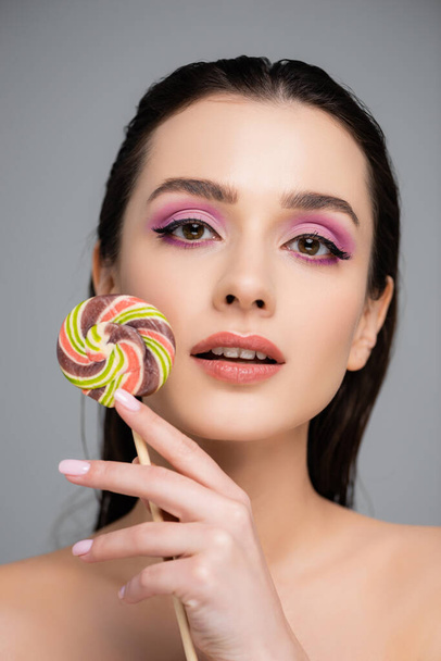 young woman with pink eye shadows holding lollipop isolated on grey  - Фото, изображение
