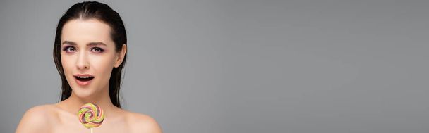 yllättynyt nuori nainen vaaleanpunainen luomivärejä tilalla tikkari eristetty harmaa, banneri - Valokuva, kuva