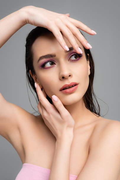 young woman with pink eye shadows and bare shoulders touching face isolated on grey  - 写真・画像