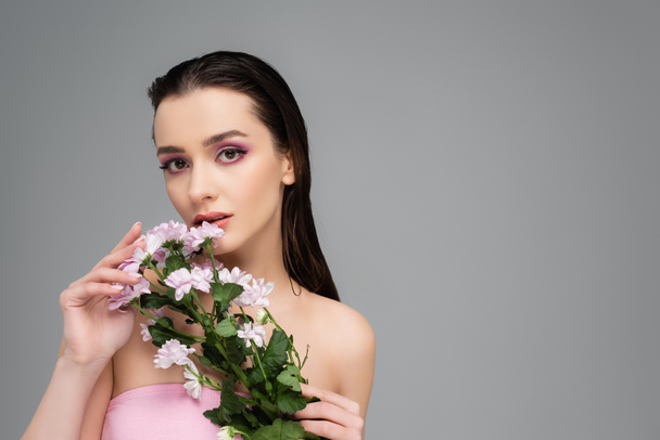 young woman with pink eye shadows holding flowers isolated on grey  - 写真・画像