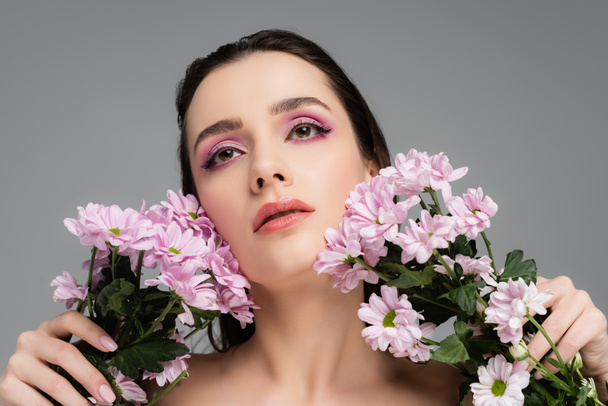 fiatal nő rózsaszín szem árnyék gazdaság virágok és felnéz elszigetelt szürke  - Fotó, kép
